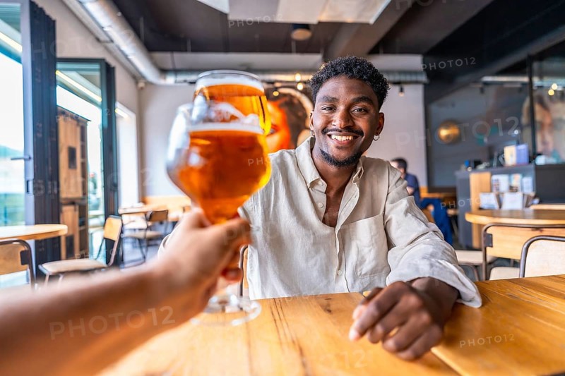 Waiter serving a refreshing glass of beer to a smiling young man in a stylish modern pub, creating a cheerful atmosphere for socializing