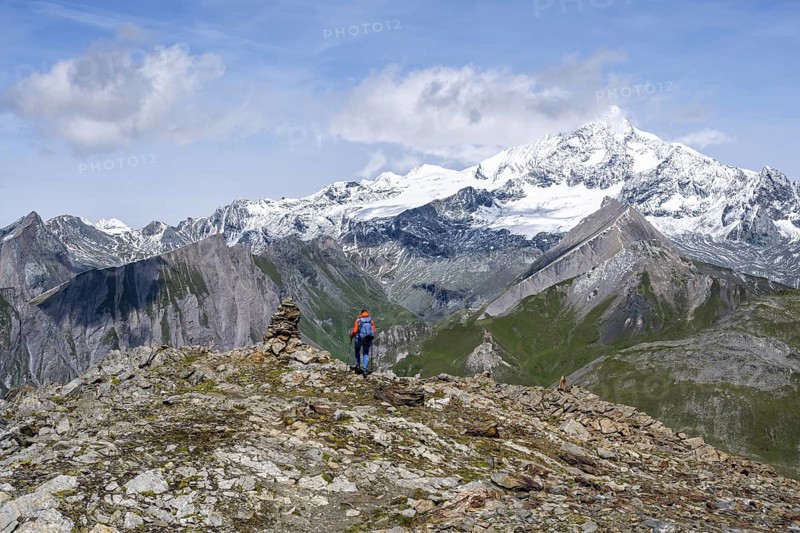 Female mountaineer on hiking trail with cairn, behind glaciated and snow-covered summit of the Großglockner, Wiener Höhenweg, Schober group, Hohe Tauern National Park, Carinthia, Austria
