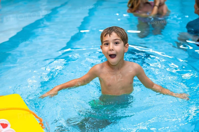 Young boy enjoying his summer vacation, playing and making funny faces in a swimming pool with a yellow kickboard