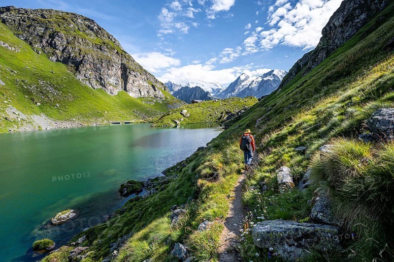 Mountaineer on a hiking trail at a mountain lake with a view of glaciated mountain peaks, Lac du Louvie with summit Grand Combine, Valais Alps, Val de Bagnes, Valais, Switzerland