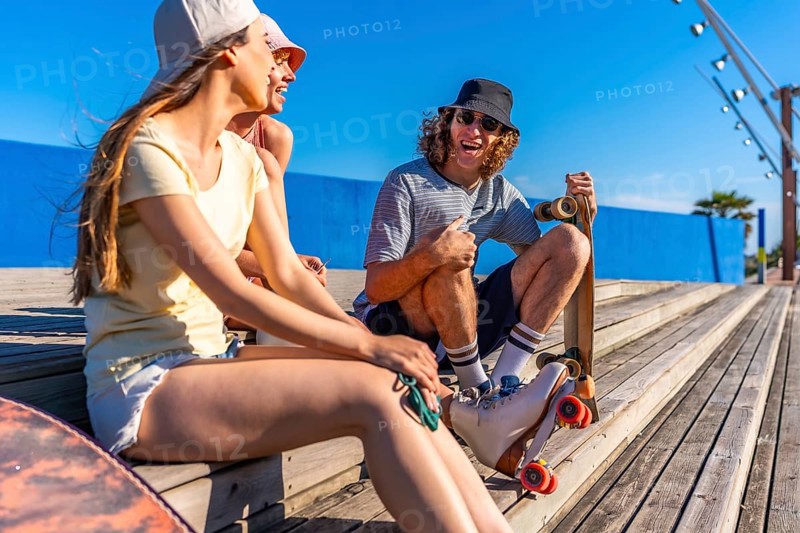 Group of young friends relaxing on wooden steps, enjoying a sunny day with skateboards, embodying a carefree and active lifestyle