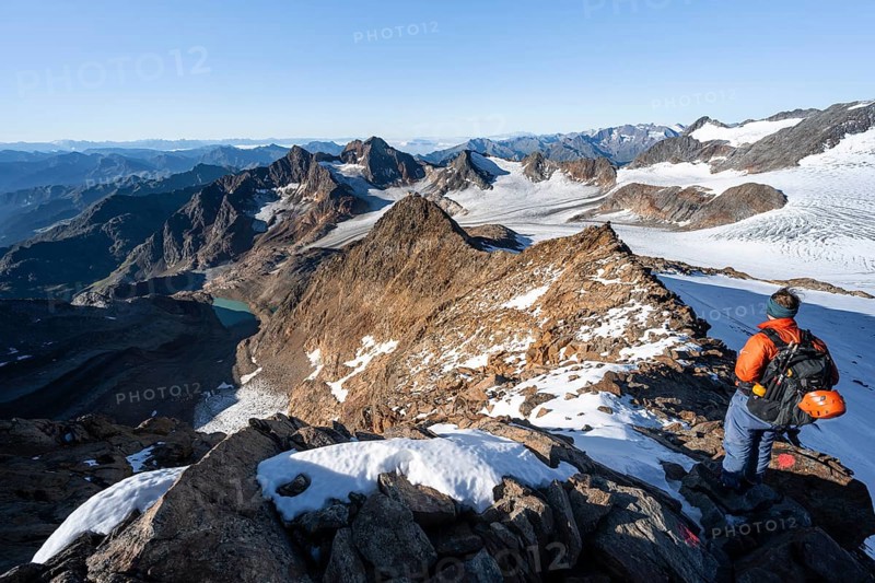 Mountaineer on a rocky ridge on the Wilder Freiger summit, behind him Signal summit and Becher summit with Becherhaus, picturesque high mountain landscape, view of Übeltalferner glacier and rocky mountain peaks Königshofspitz and Sonklarspitze, Stubai Alps, South Tyrol, Italy