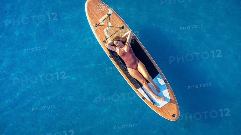 Lying on a paddle board, a woman enjoys the tranquility of the calm blue sea, soaking up the sun and embracing the peaceful summer vibes