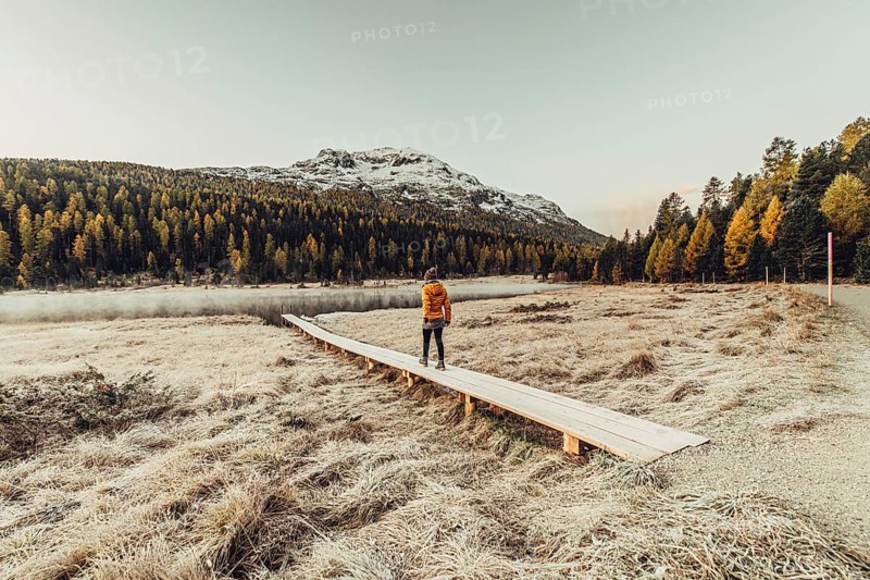 Young woman at Lake Staz near Sankt Moritz in the Engadine in Switzerland. Morning atmosphere with fog in autumn. Reflection of water