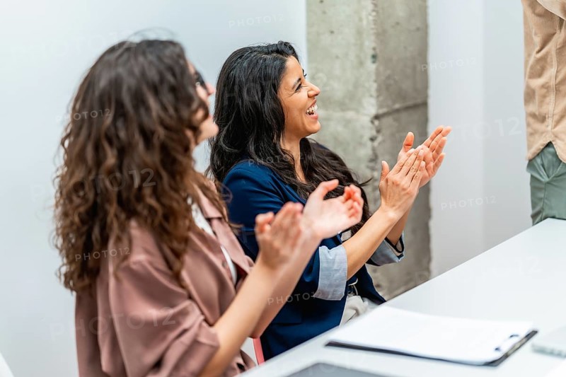 Two businesswomen clapping hands and smiling during a business meeting, showing appreciation and support for a colleague