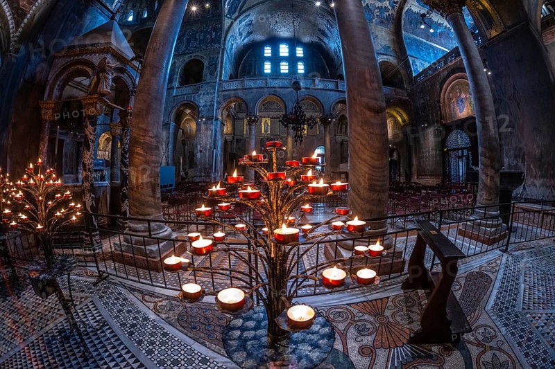 Several burning votive candles create a warm glow in the basilica di san marco, showcasing the intricate details of its architecture