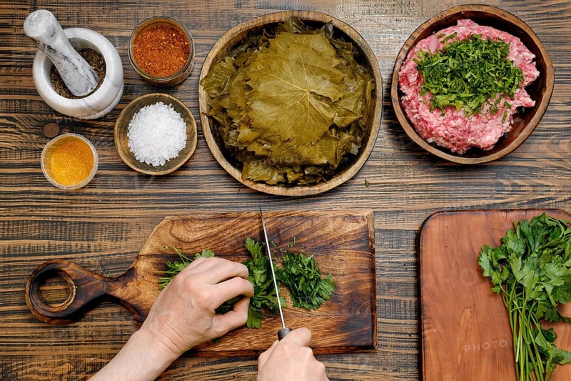 Preparing traditional dolma involves chopping herbs and meat, spreading grape leaves, and mixing spices in a cozy kitchen