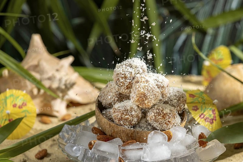 Coconut flakes fall on almond and chocolate confectionery in a coconut on ice cream with umbrellas on sand