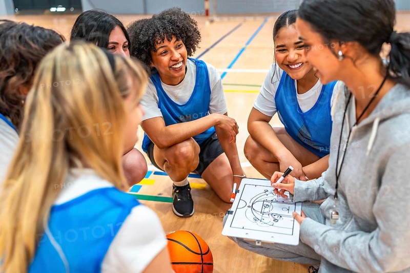 Female basketball coach drawing a play on a clipboard while explaining game strategy to her team during a time out