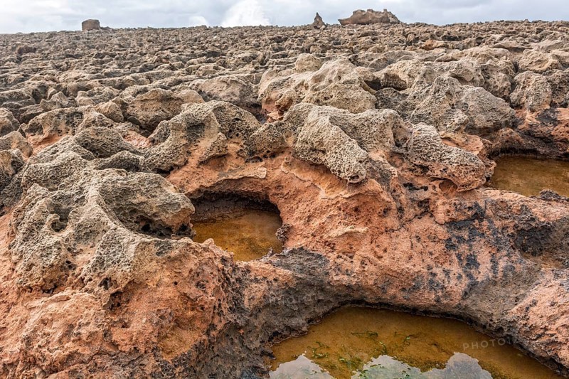 A rocky area with a hole in the ground. The hole is filled with water. The water is brown in colour. Rabat, Morocco
