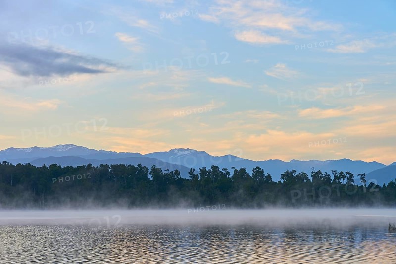 A peaceful lake with a misty surface and mountains in the morning light, Lake Mahinapua, Ruatapu, South Island, New Zealand