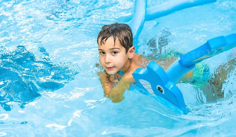 Happy boy enjoying playtime with an inflatable toy whale in a sparkling swimming pool, soaking up the sun during summer vacation