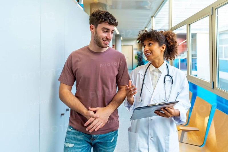 Doctor holding clipboard and explaining diagnosis to patient while walking in hospital corridor