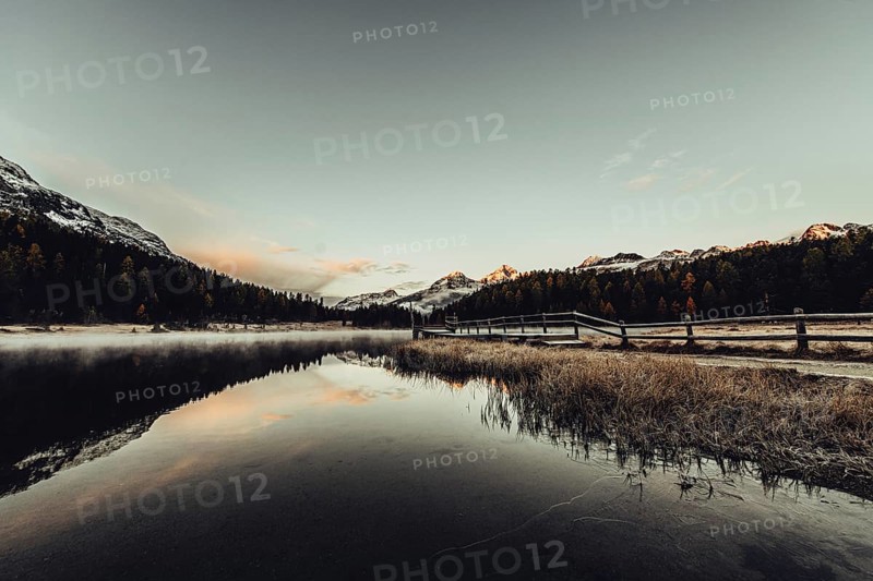 Lake Staz near Sankt Moritz in the Engadin in Switzerland. Morning atmosphere with fog in autumn. Water reflection and snow-covered mountains in the background