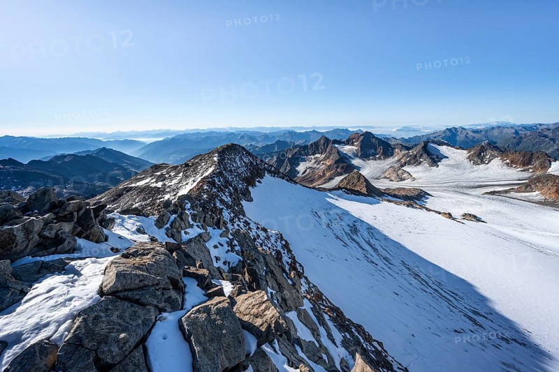 Narrow rocky ridge at the Wilder Freiger summit, picturesque high mountain landscape with snow, view of Übeltalferner glacier and rocky mountain peaks Königshofspitz and Sonklarspitze, Stubai Alps, South Tyrol, Italy