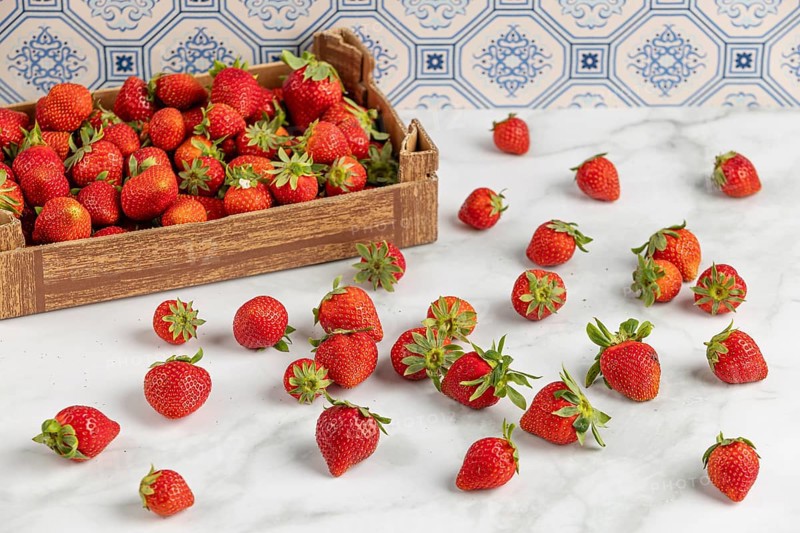Strawberries scattered on a marble slab, next to a box full of strawberries