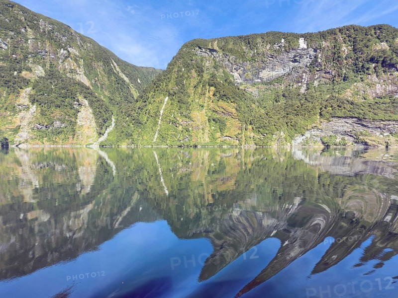 Mountains with reflections in the water against a blue sky in Doubtful Sound, South Island, New Zealand, Oceania