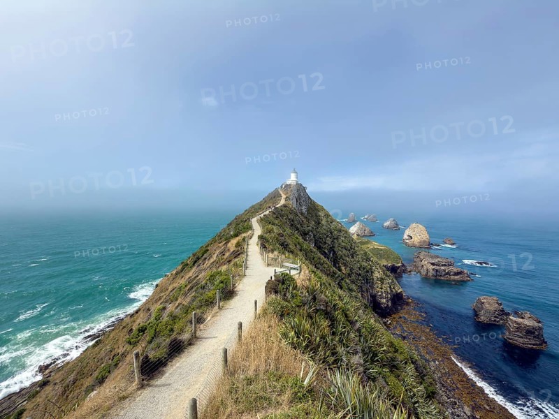Nugget Point Lighthouse with Nugget Rocks in front of a blue sky, South Island, New Zealand, Oceania