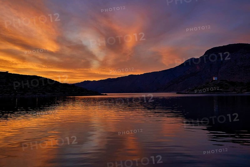 Colourful sunset over a calm lake with mountainous backdrop, Holy Week, Bay of Panormitis, Panormitis Monastery, Symi, Dodecanese, Greek Islands, Greece