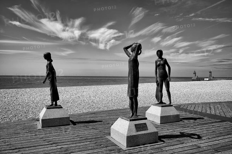 Bronze sculpture La Heure du Bain by Dominique Denry on the beach, sky, blue, behind it beacon Feu de la jetée Sud, lighthouse, Phare de Fécamp, harbour entrance, Fécamp, Normandy, Seine-Maritime, France