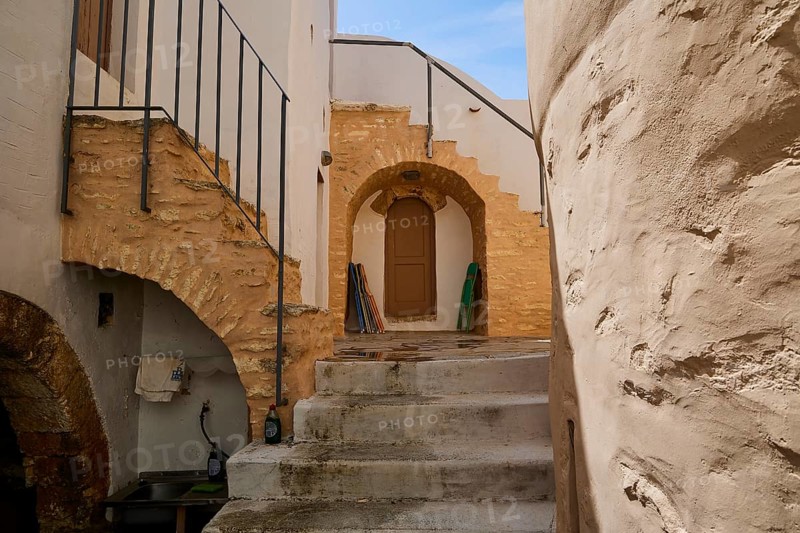 Historic courtyard with stairs, stone arches and wooden doors in the sunlight, Monastery, Moni Roukouniotis, Symi, Dodecanese, Greek Islands, Greece