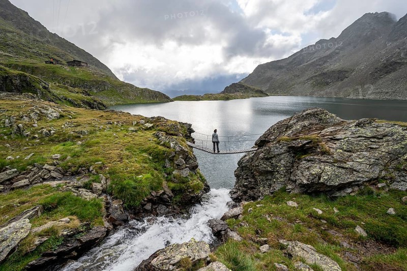 Mountaineer standing on a suspension bridge, mountain stream and mountain lake Wangenitzsee, Schober Group, Hohe Tauern National Park, Carinthia, Austria