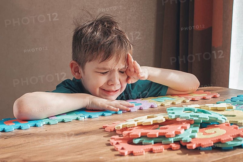 Boy with autism, expresses frustration, playing with puzzle pieces, on a wooden table, natural light, lifestyle