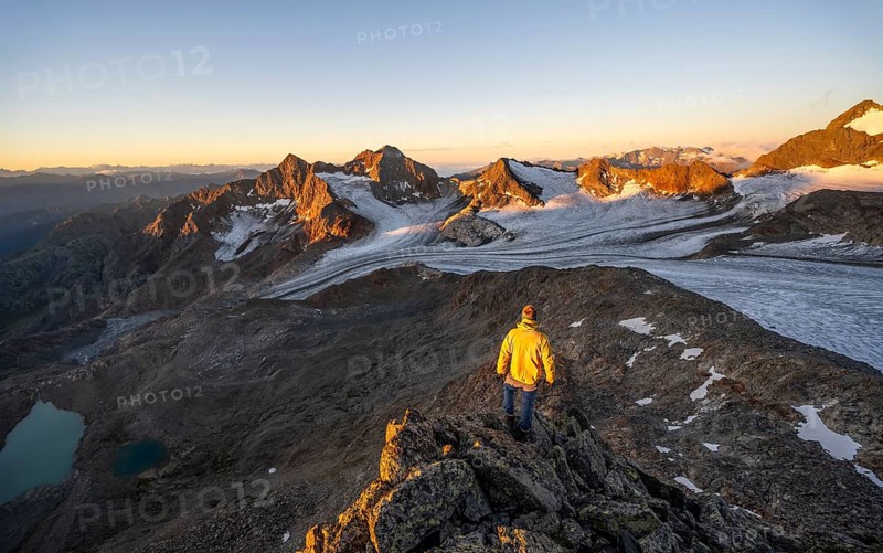 Mountaineers in front of a picturesque high mountain landscape at sunrise with alpenglow, blue glacial lakes, glaciers and rocky mountain peaks in the morning light, view at the Becher on mountain peaks Königshofspitz and Sonklarspitze and Schwarzwandspitz with glacier Übeltalferner, Stubai Alps, South Tyrol, Italy