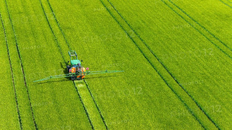 Farmer with tractor working in the field. In early summer, he fertilises the grain for an optimum yield. Drone photo. Merklingen, Baden-Württemberg, Germany