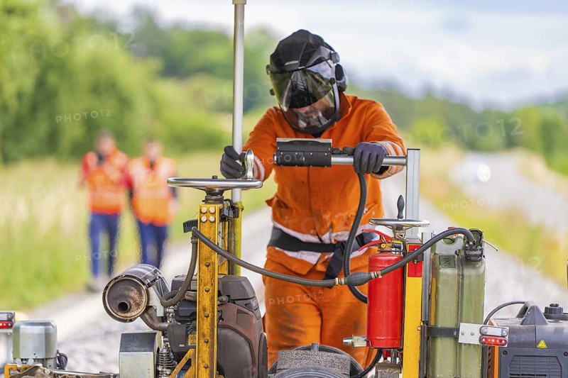 Welder on railway track, surrounded by machines, in the middle of a job, grinding work on the Hermann Hesse railway, Ostelsheim, district of Calw, Germany