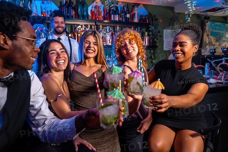 Cheerful group of friends raising glasses of mojito cocktails, enjoying nightlife at a vibrant bar