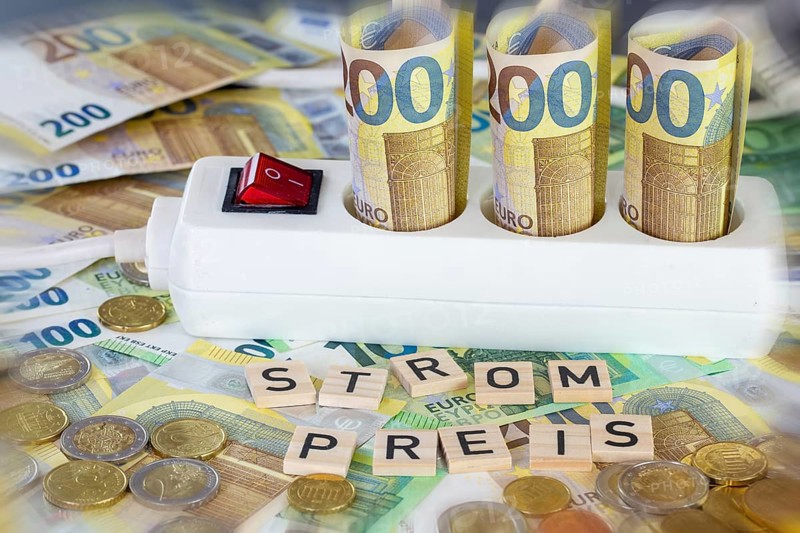 Symbolic image of electricity costs: multiple socket with euro banknotes and euro coins, with the word STROMPREIS in wooden letters in front of it