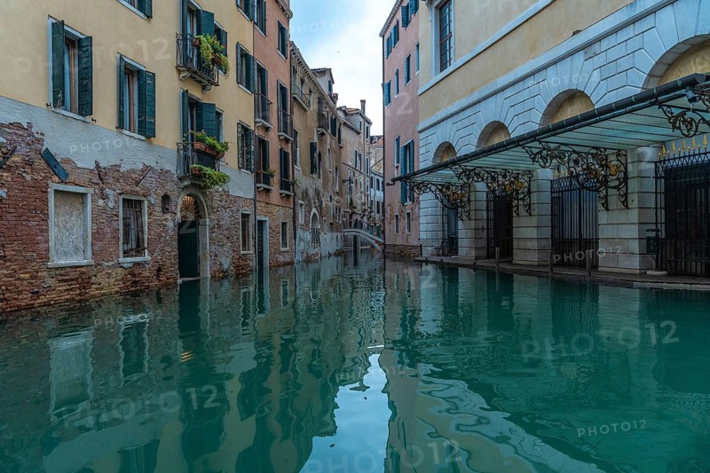 Calm water reflecting colorful buildings along a canal in venice, italy, during acqua alta, or high tide