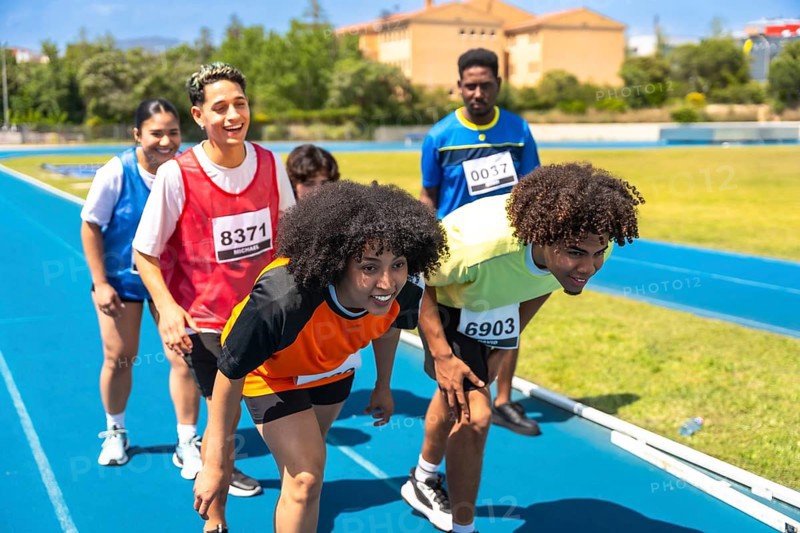 Diverse group of athletes crouching at starting line, preparing for a race on a blue running track