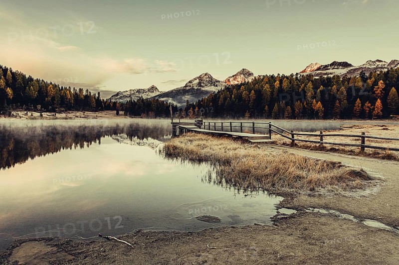 Lake Staz near Sankt Moritz in the Engadin in Switzerland. Morning atmosphere with fog in autumn. Water reflection and snow-covered mountains in the background