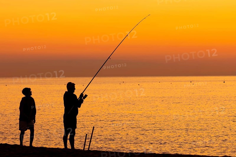 A man fishing just in front of sunrise on the Costa Rei, a coastline of the Italian island of Sardinia, in the Mediterranean Sea, Monte Nai, Costa Rei, Sardinia, Italy