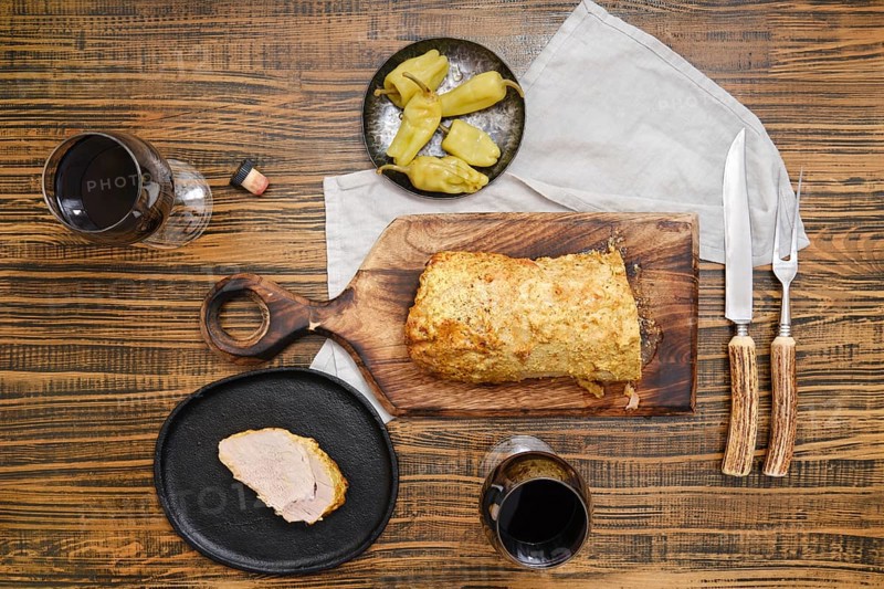 Overhead view of roasted pork meat and pickled peppers on a wooden table accompanied with red wine in glasses