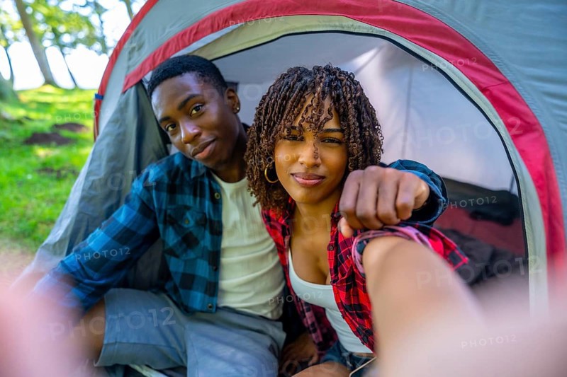 Young couple smiling and taking a selfie inside their cozy tent, enjoying a delightful camping trip surrounded by nature's beauty
