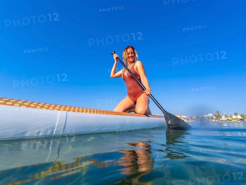 Young woman paddling on a stand up paddle board on a sunny summer day, enjoying the calm blue water