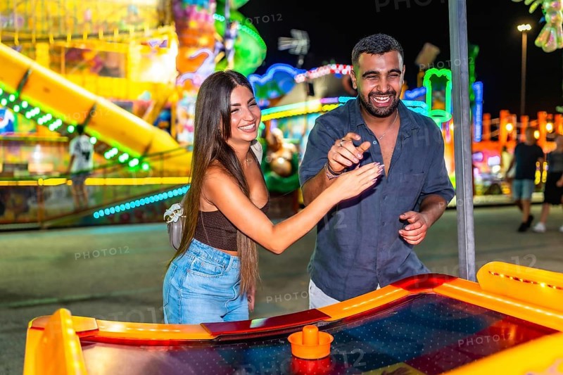 Young couple enjoying a game of air hockey at a brightly lit amusement park, adding excitement to their night out