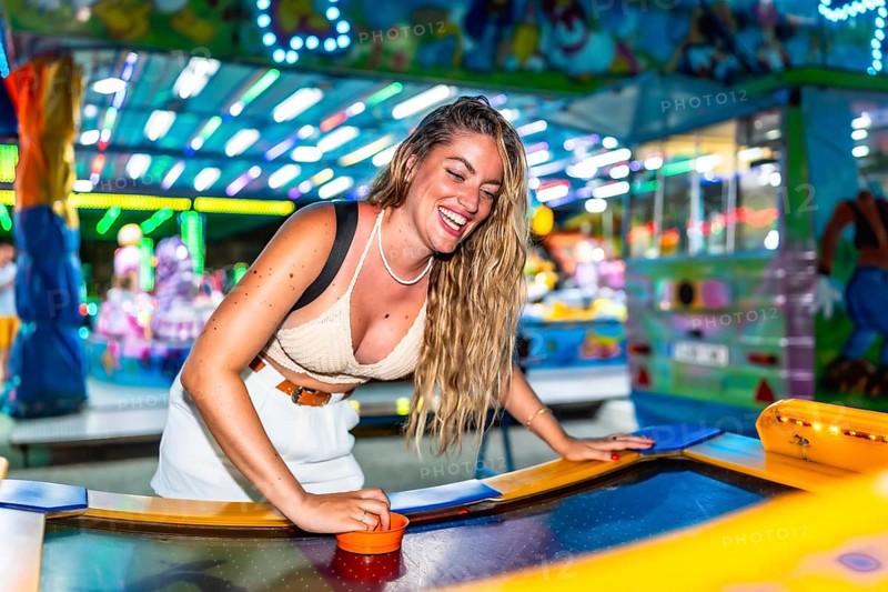 Young woman enjoying a game of air hockey at a brightly lit amusement park, laughing and having a good time