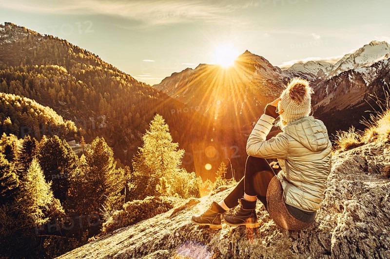Woman sitting thoughtfully at a feslen at autumn atmosphere during sunset in the Swiss Alps in the Engadine. Photographed from the village of Maloja on the Maloja Pass