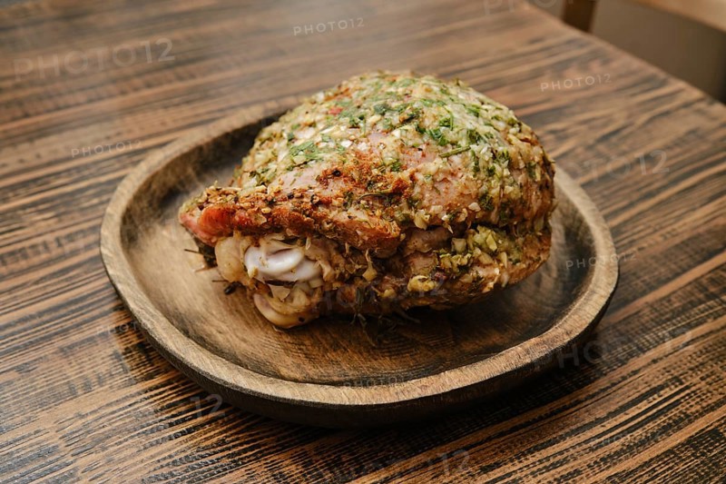 A roasted turkey thigh on a round wooden plate. The thigh is seasoned with fresh herbs, showcasing its crispy skin and juicy meat, perfect for a festive dinner or gathering