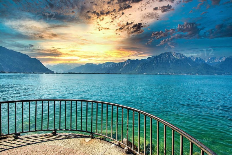 Golden light reflects on the calm waters of Lake Leman as clouds gather over the mountains in Montreux. A tranquil evening captures the charm of Canton de Vaud, Switzerland