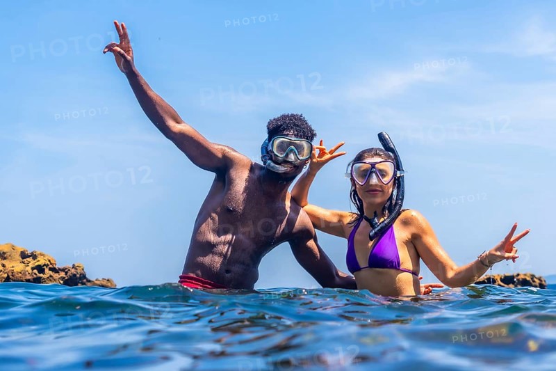 Young multi ethnic couple wearing snorkeling masks and enjoying summer vacation in tropical sea making victory hand gesture