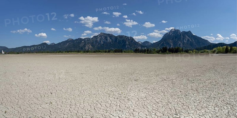 Cracked, dried out ground, waterless Forggensee in spring, behind it Tegelberg massif and Säuling, Ammergau Alps, near Füssen, Ostallgäu, Bavaria, Germany
