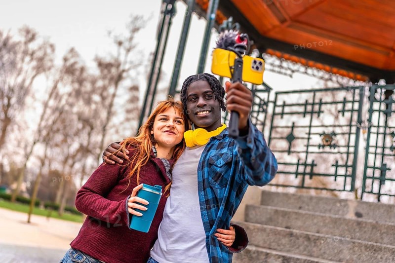 Two young content creators are recording a video blog in a park, using a smartphone attached to a gimbal with external microphone