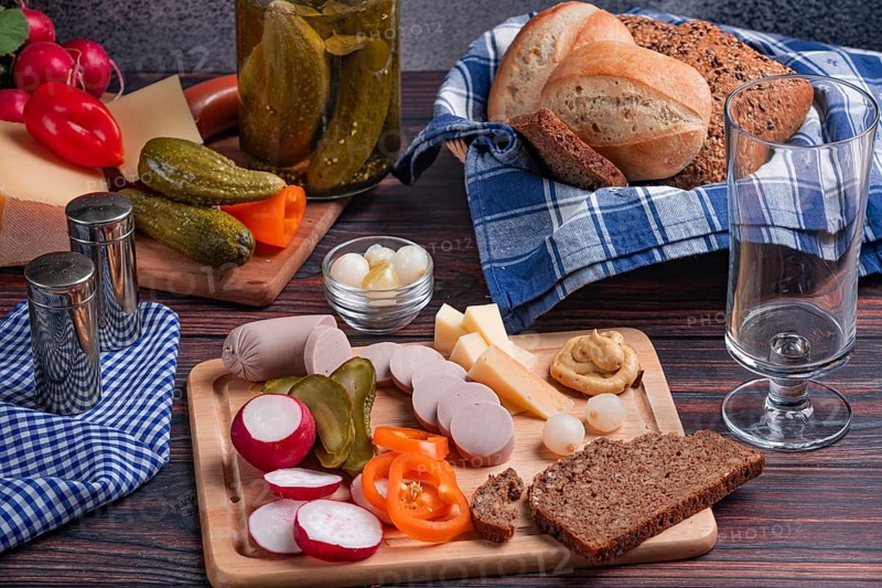Rustic snack with sausage, cheese, vegetables, mustard and bread on a laid table