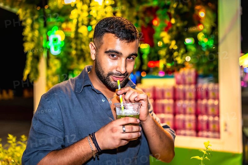 Young man sips a mojito through a straw at a vibrant night market, enjoying the festive atmosphere