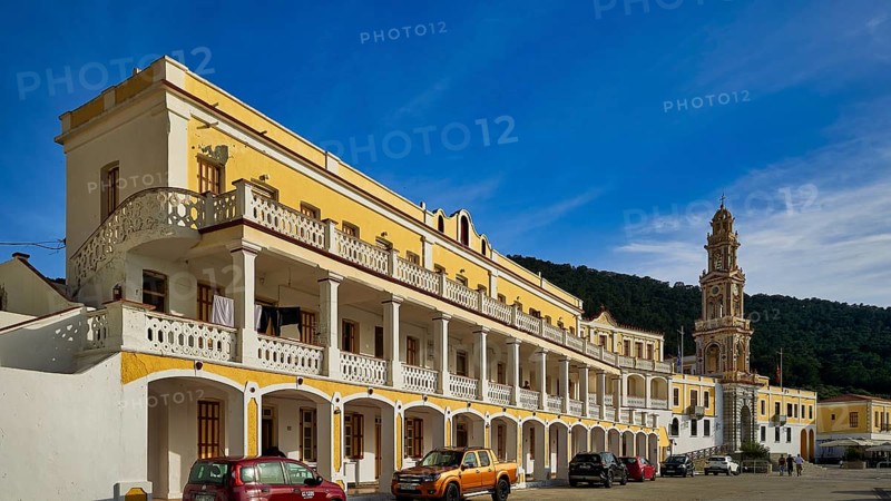 Yellow building with balconies, vehicles in front, blue sky in the background, Holy Week, Bay of Panormitis, Panormitis Monastery, Symi, Dodecanese, Greek Islands, Greece